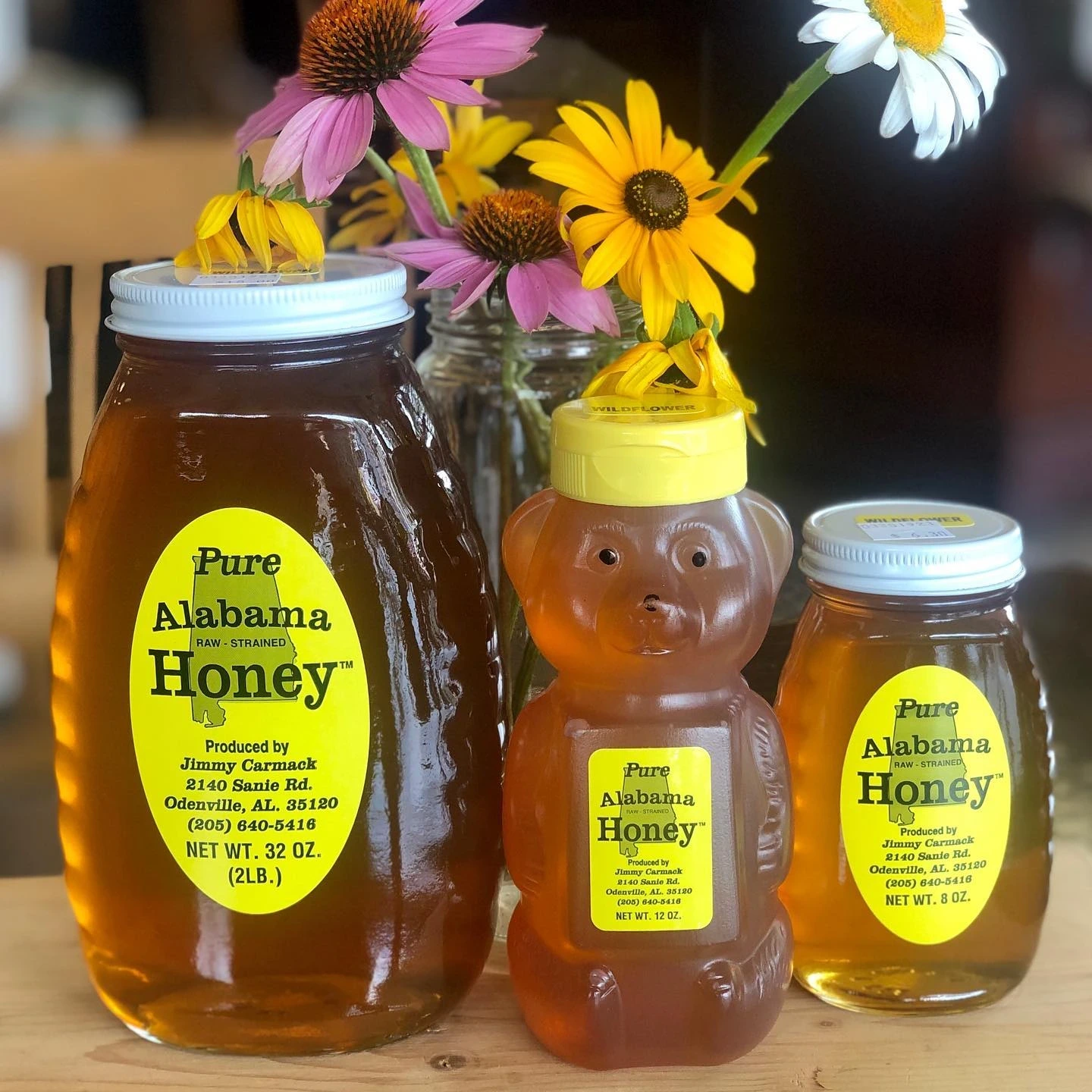 Three bottles of local Alabama honey in front of wildflowers