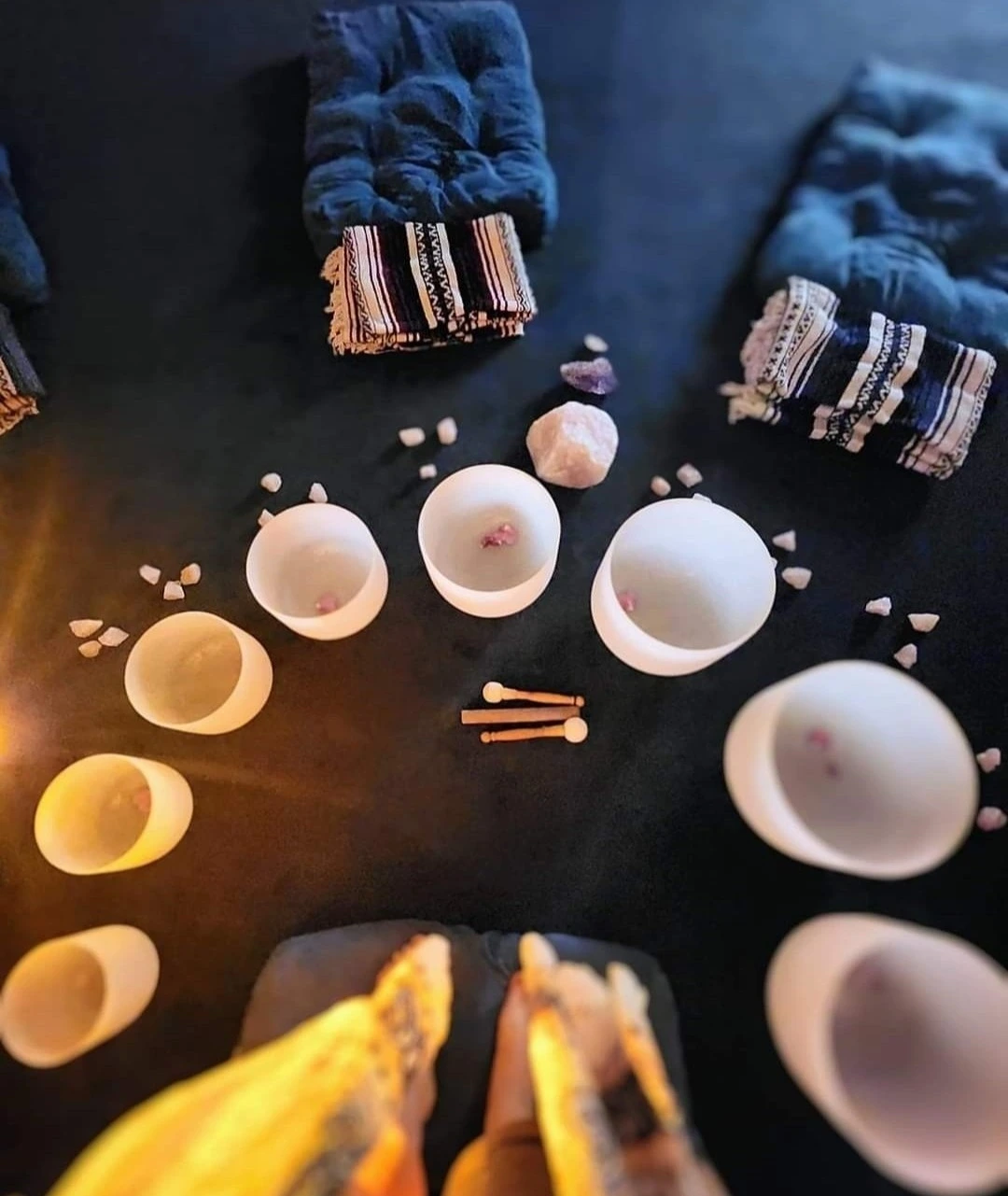 Several white glass singing bowls in a semi-circle, surrounded by blankets and candles