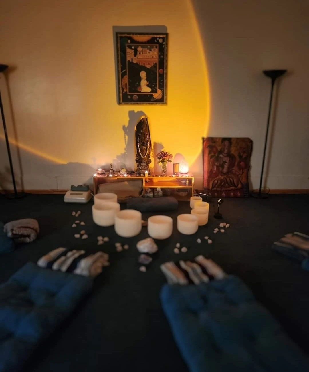 An altar with statues, candles, incense, and surrounded by singing bowls and blankets